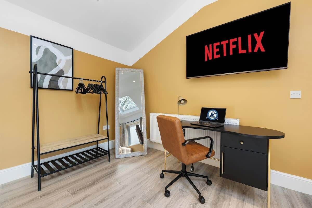 Une pièce comprenant un bureau, une chaise et un téléviseur fixé au mur qui affiche le logo « NETFLIX ».