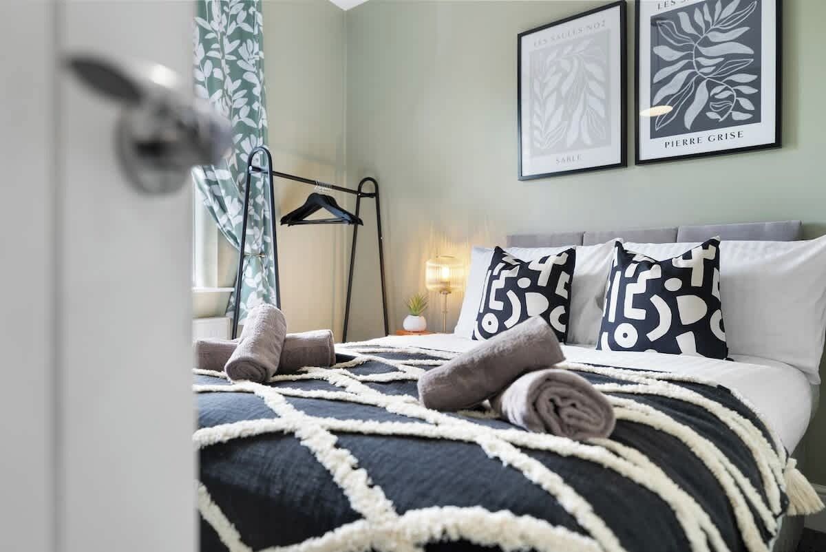 Un letto rifatto con cuscini decorati, un appendiabiti a parete e quadri incorniciati.
