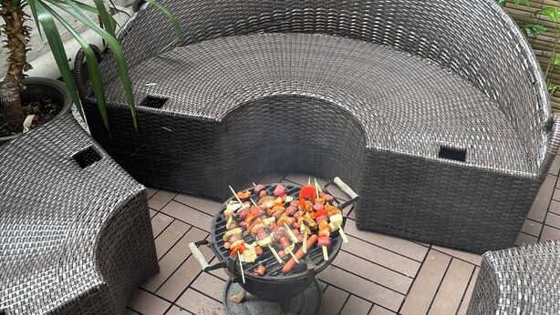 Un área de estar al aire libre con muebles de mimbre y una parrilla en el centro.