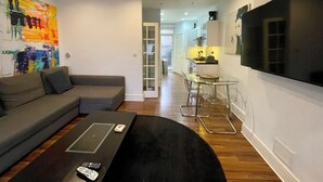 Una sala moderna con un sofá gris, una mesa de comedor de vidrio con sillas, una mesa de centro negra y un televisor montado en la pared.