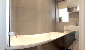 Bathroom features a curved bathtub, large mirror, and a potted plant.