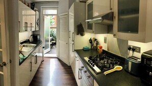 Cocina estrecha con estufa a gas, tostadora y lavamanos. Hay una puerta que da a un patio.