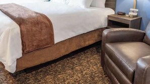 A hotel room with a large bed, a brown leather armchair, a nightstand with a lamp, and a framed picture on the wall. - Cozy 1-bedroom hotel in delightful Huntersville up to 2 people (Huntersville)