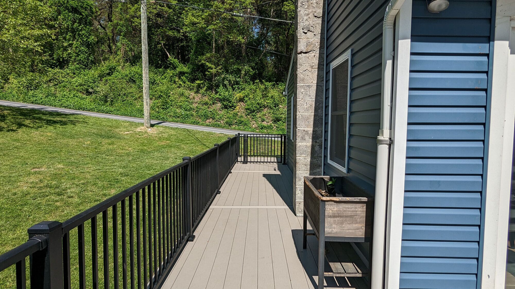 A wooden deck with a black railing, leading to a house with blue siding.