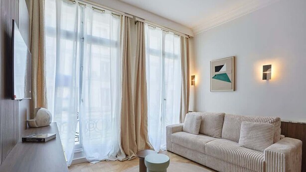 A modern living room with a sofa, a round coffee table, and a TV on a wooden cabinet. - Superb Apartment on the Champs Elysees (Paris)