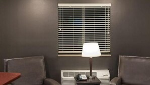 Una habitación con dos sillones de cuero, una mesita con una lámpara, un calentador y una ventana con persianas.
