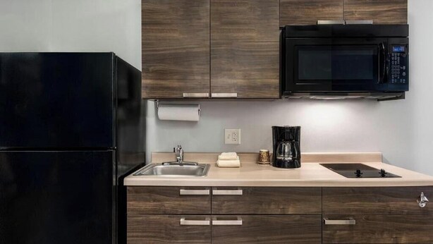 Una cocina moderna con armarios de madera oscura, un refrigerador negro, un microondas, un lavamanos y una cafetera.