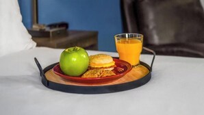Bandeja de desayuno con una manzana verde, una galleta y un vaso de jugo de naranja sobre una cama.