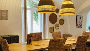 Un coin repas avec des meubles en osier, deux lampes suspendues et une vue sur l’extérieur par une fenêtre.