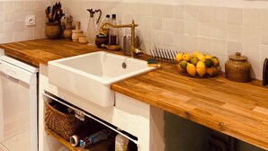 Une cuisine dotée d’un plan de travail en bois, d’un évier blanc et d’un luminaire suspendu en osier.
