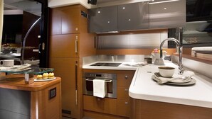A modern kitchen with wooden cabinetry, stainless steel appliances, and a glass island counter. - Luxurious 55-Foot Yacht with Captain & First Mate (Sarasota)