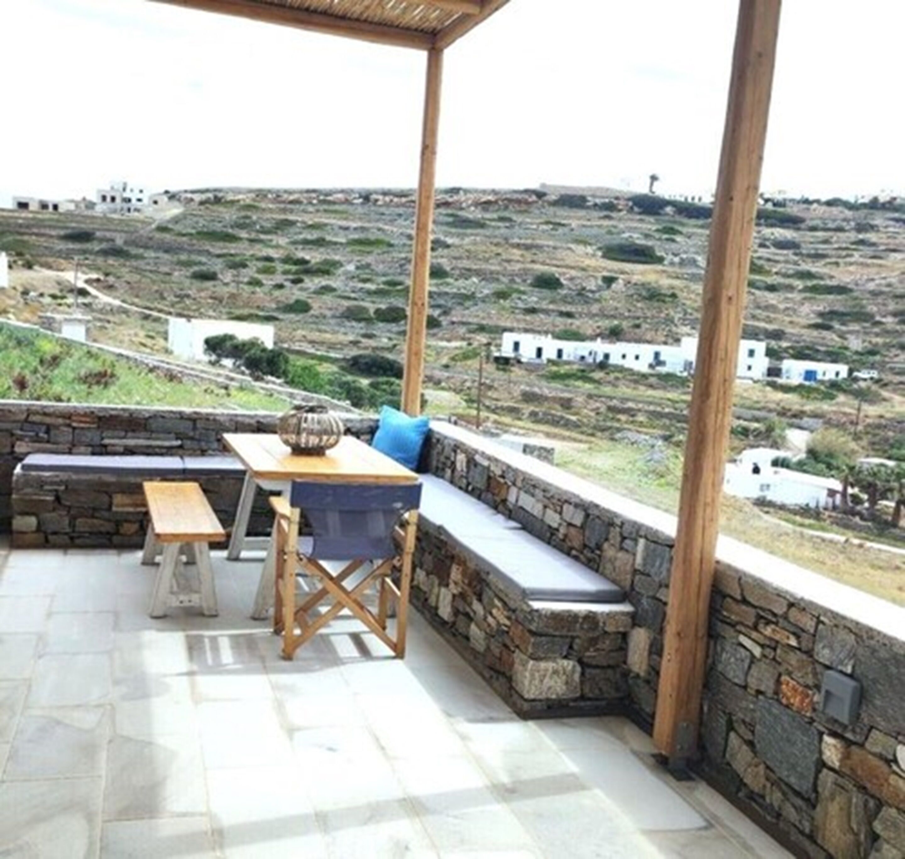 Un área de estar al aire libre con una mesa y bancos, con vistas a un paisaje montañoso con edificios blancos.