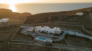 Vista aerea di una proprietà costiera con piscina, diversi edifici e una strada che conduce al mare.