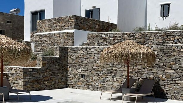 Un edificio moderno con piscina, pareti in pietra e ombrelloni di paglia.