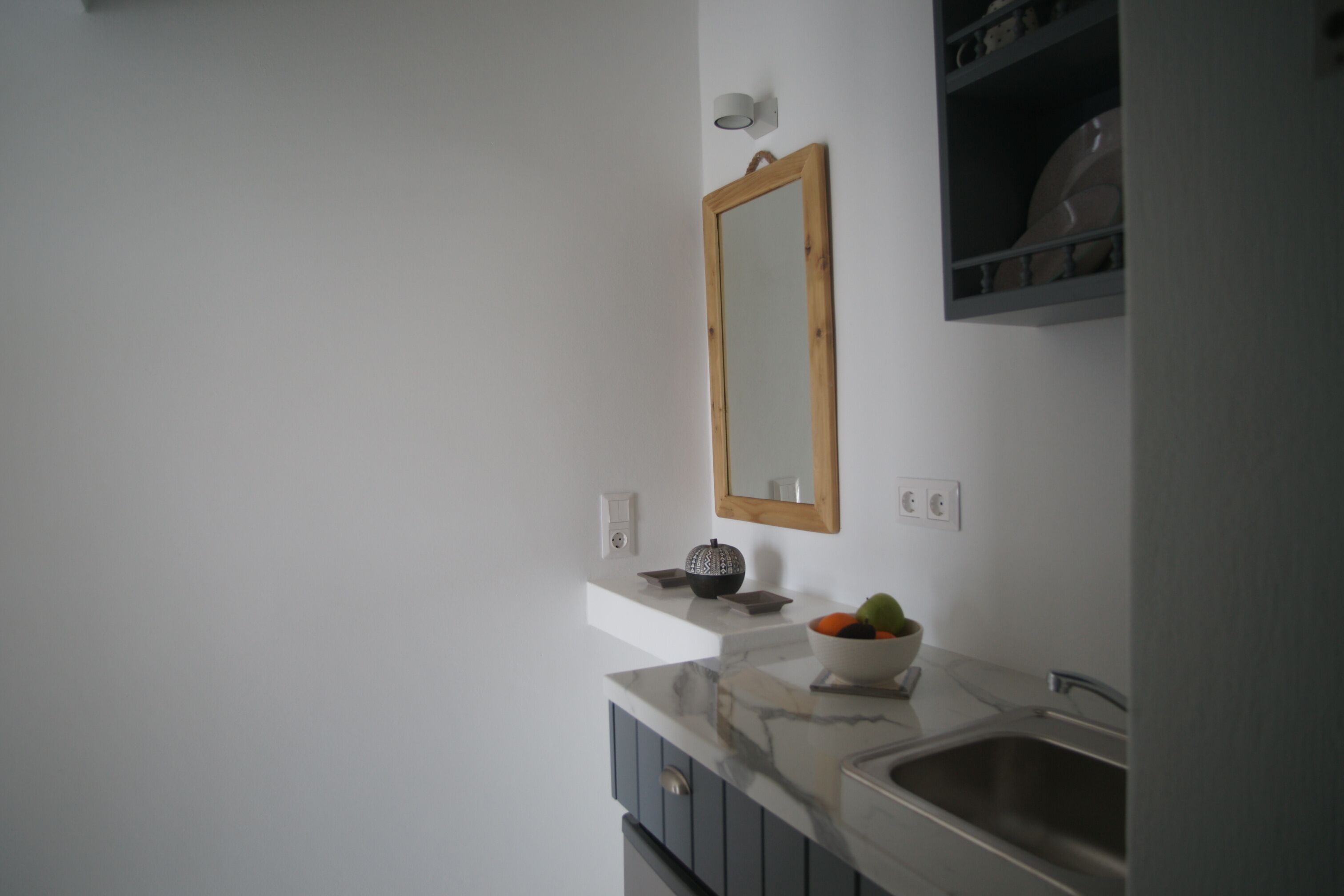 A bathroom with a white sink, a mirror, and a shelf with a bowl of fruit.