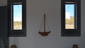 Una camera da letto con un letto, due comodini, un ornamento in legno appeso e due finestre che si affacciano su un paesaggio.