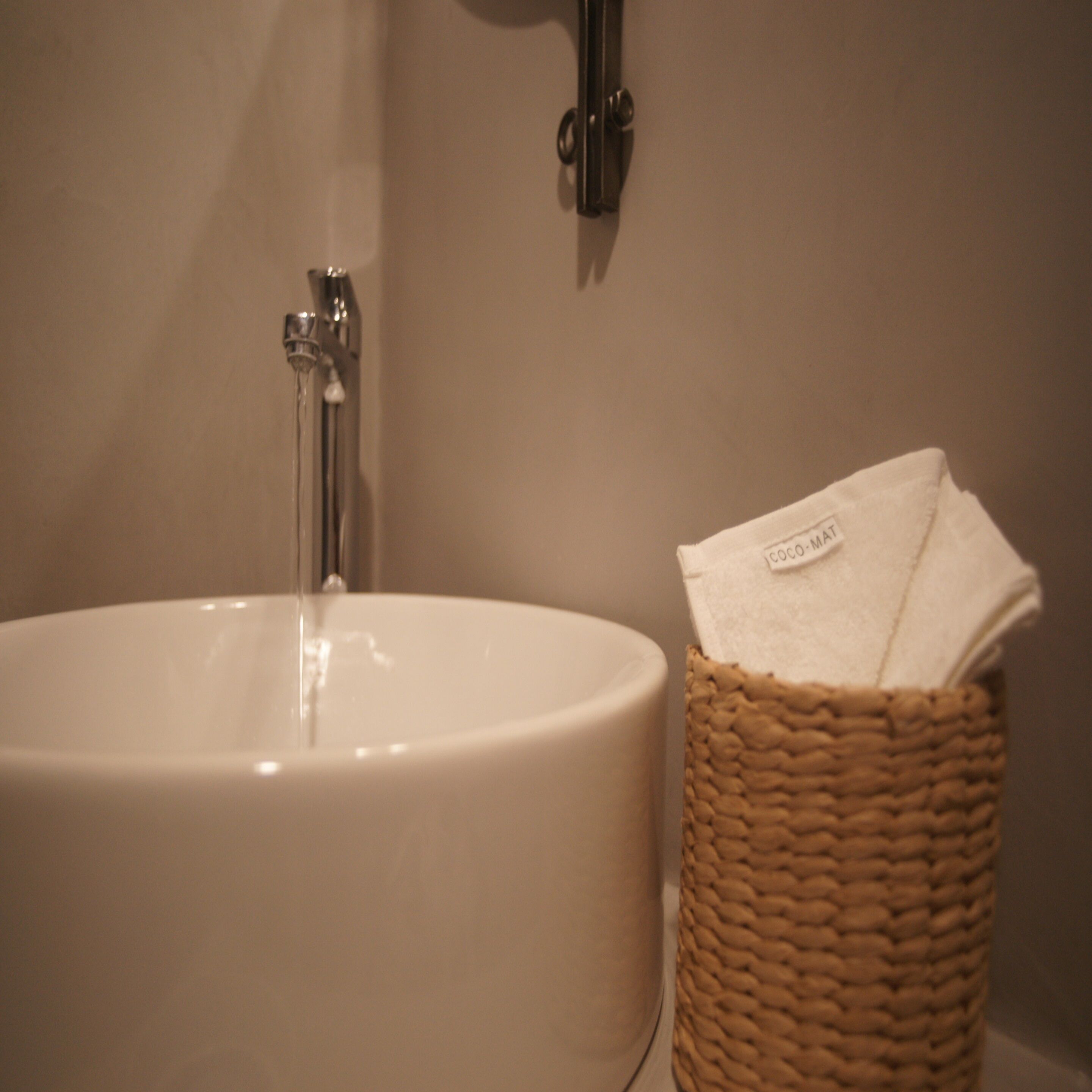 Un lavabo de salle de bain avec un robinet et un panier en osier contenant une serviette blanche.