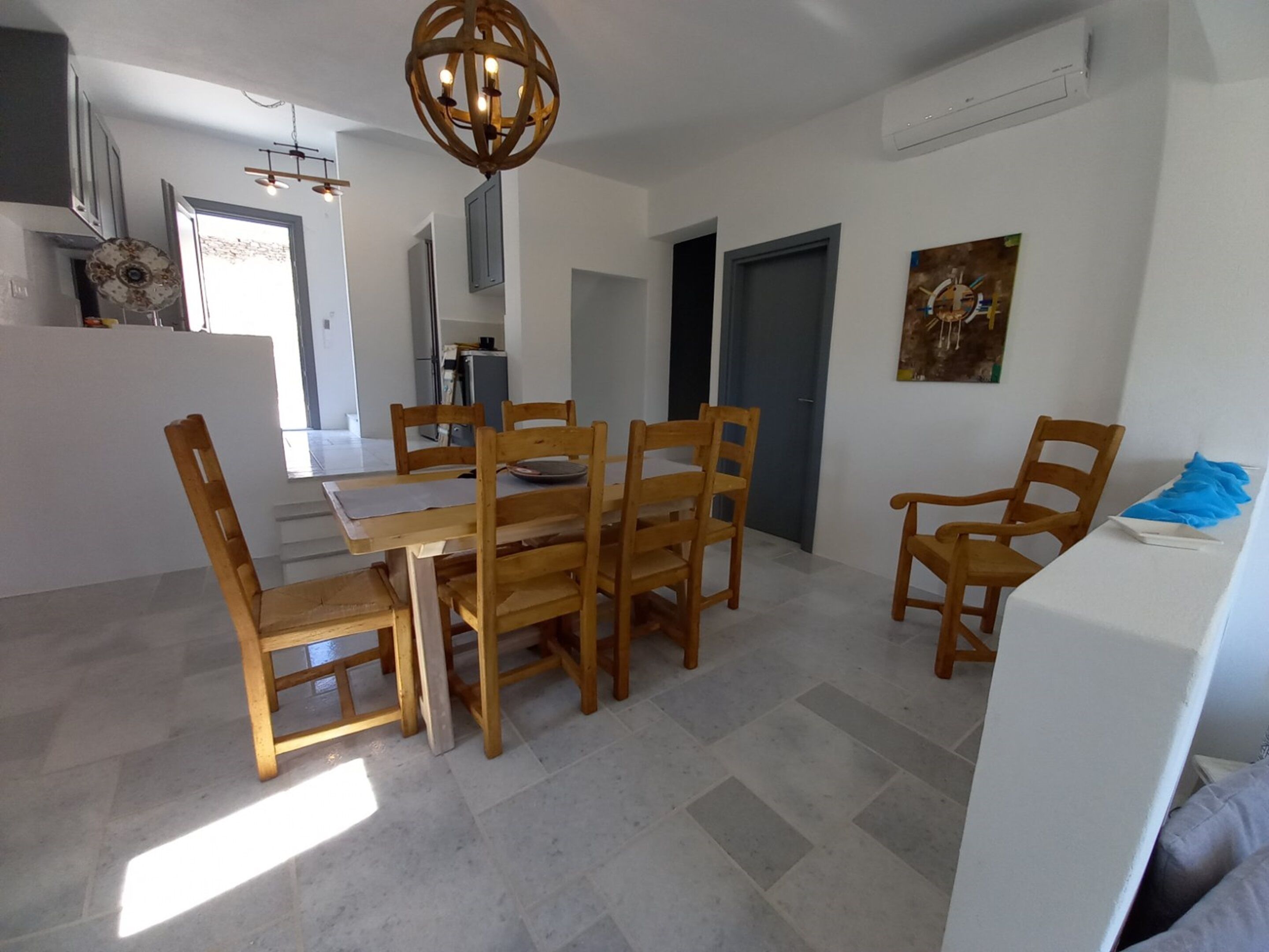 Un comedor con una mesa y sillas de madera, una araña y una cocina al fondo.