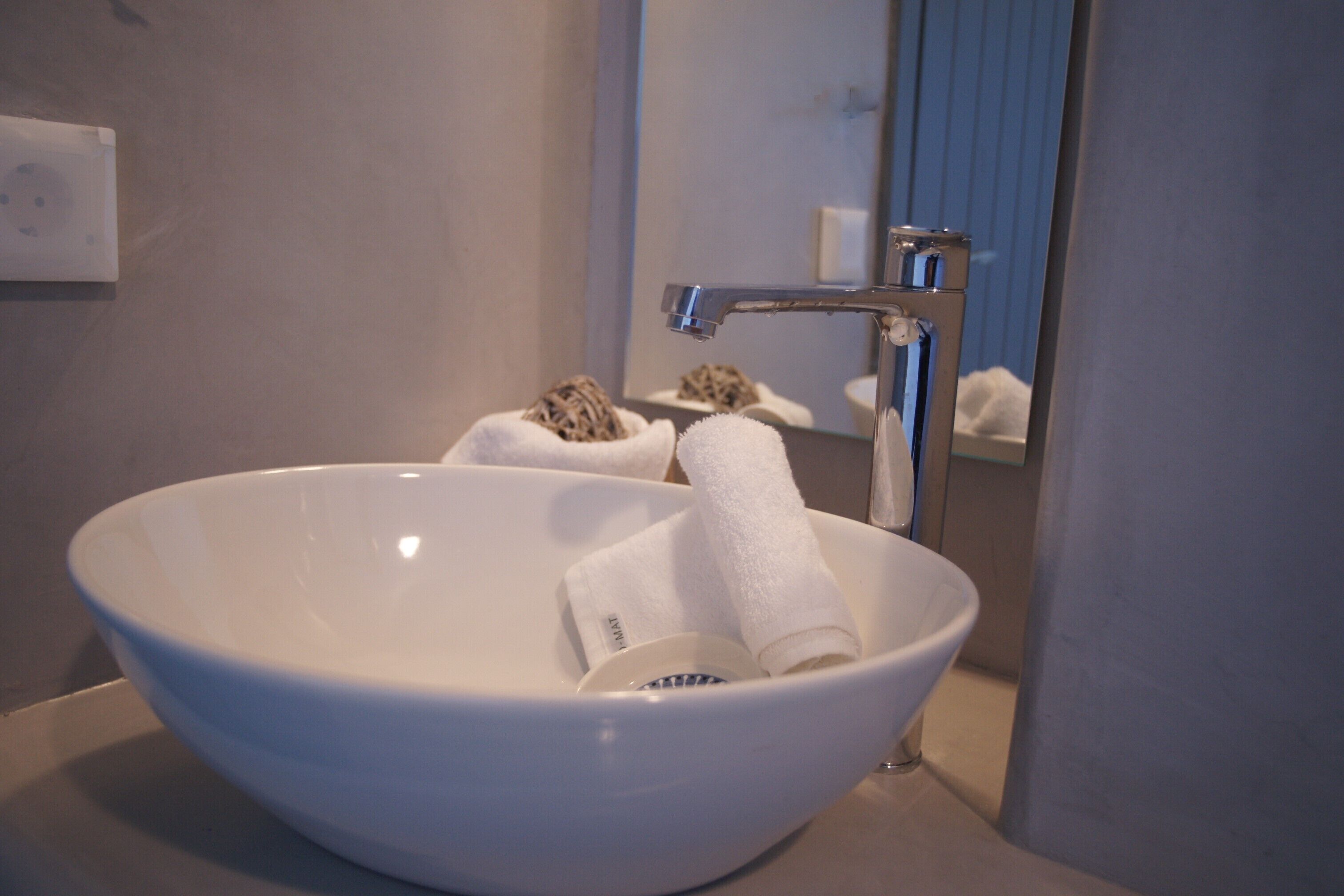 Een witte keramische wasbak met een moderne kraan, een handdoek en een zeepdispenser.
