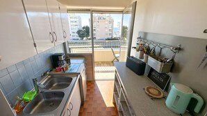 A modern kitchen with a large sink, a coffee machine, and a view of the city through the balcony.
