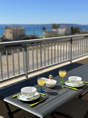 Ein Balkon mit Tisch für zwei Personen, ausgestattet mit einer Schale und einem Getränk, mit Blick auf eine Küstenlandschaft.