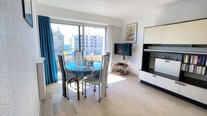 A modern living room with a dining table, a flat-screen TV, and a bookshelf.