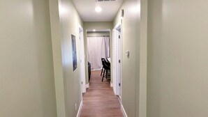 A hallway with a wooden floor and light green walls, leading to a room with a white ceiling and a window. - Sleek and Central Small Home ~ Close to everything (Flint)