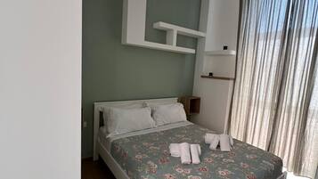 Ein Schlafzimmer mit einem Bett, einem Nachttisch, einem an der Wand befestigten Regal und einem Fenster mit Vorhängen.