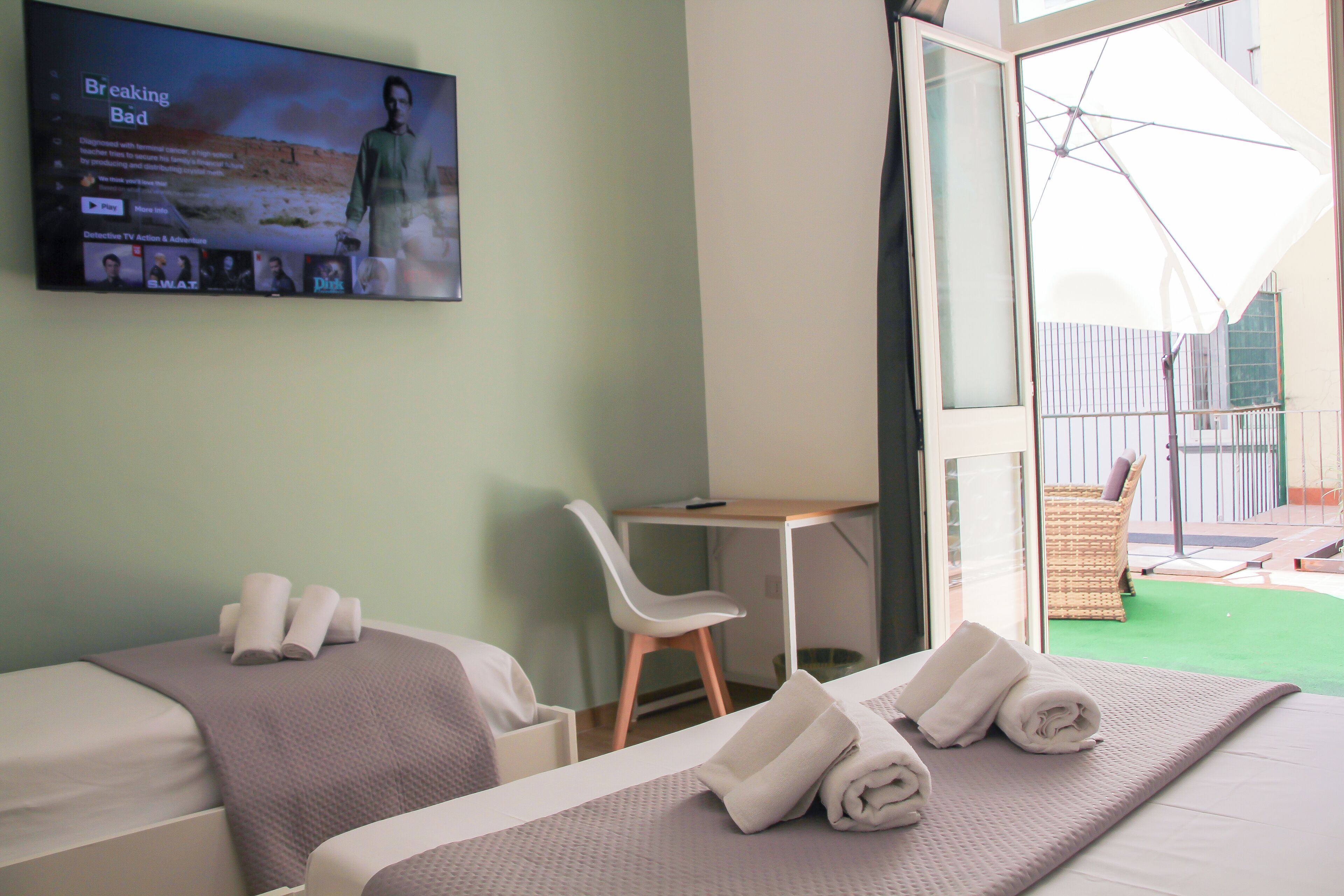 Habitación de hotel con dos camas, un escritorio y un televisor mostrando una película.