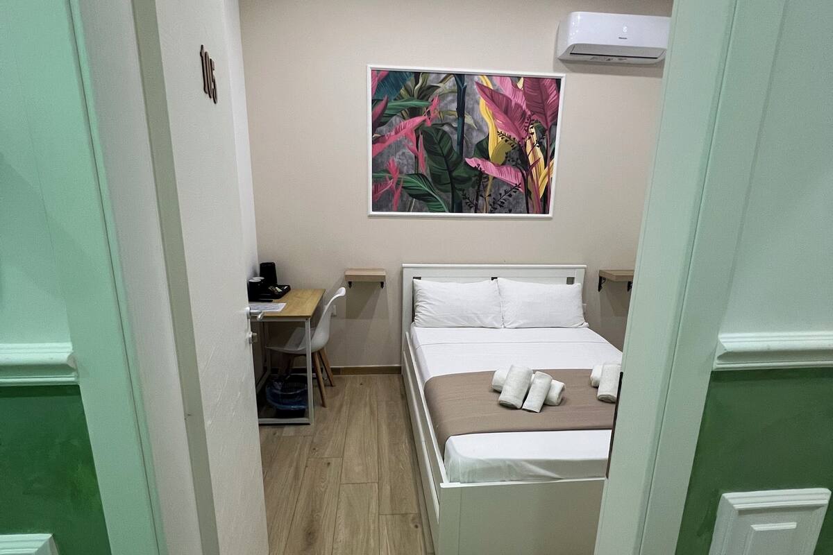 A room with a bed, a desk, and a colorful painting on the wall.