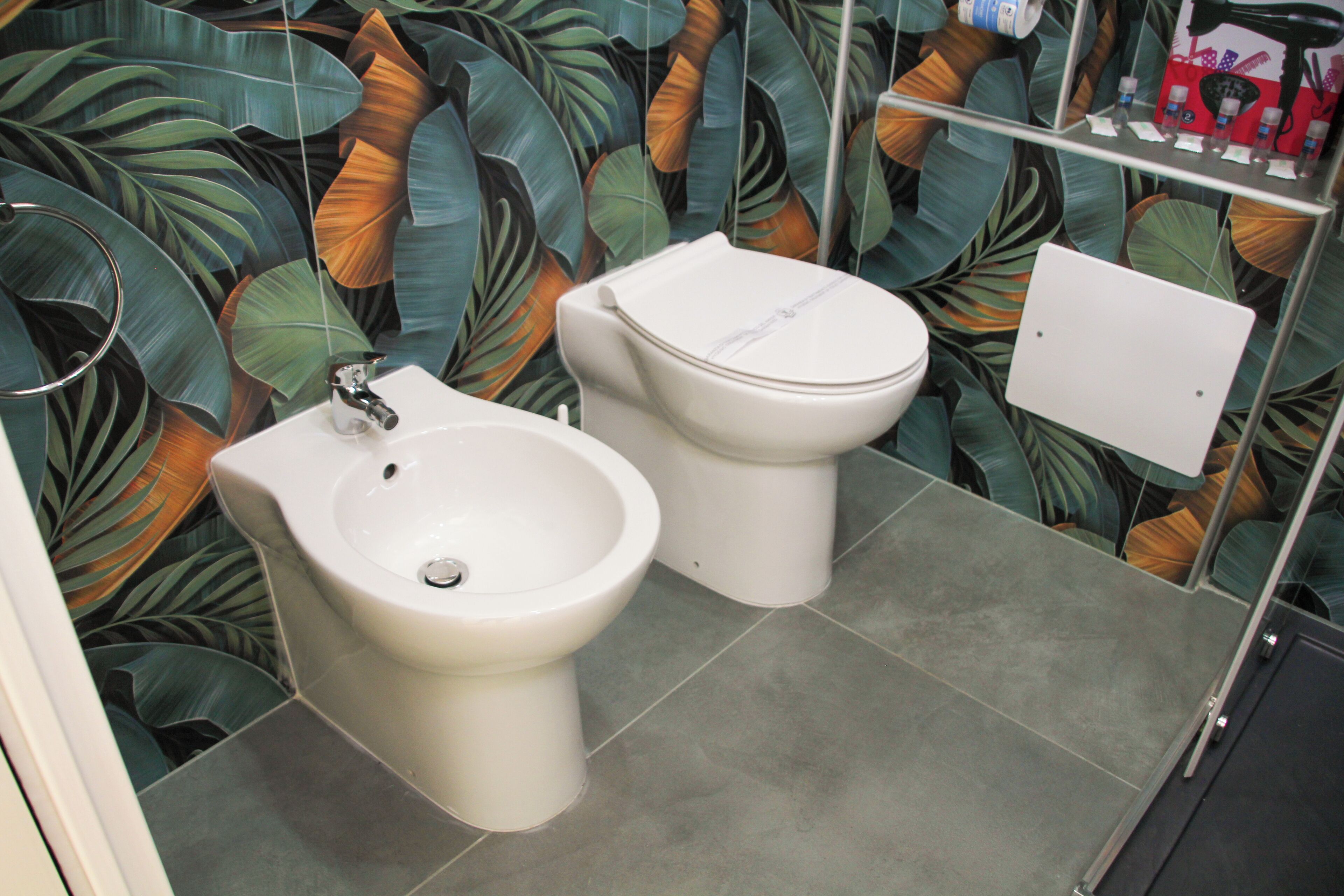A bathroom with a bidet, a toilet, and a shelf with toiletries.