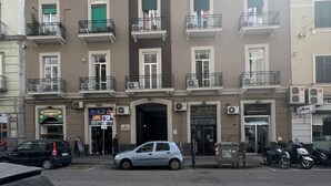 Un edificio de varios pisos con balcones, entrada a nivel de calle y vehículos estacionados.