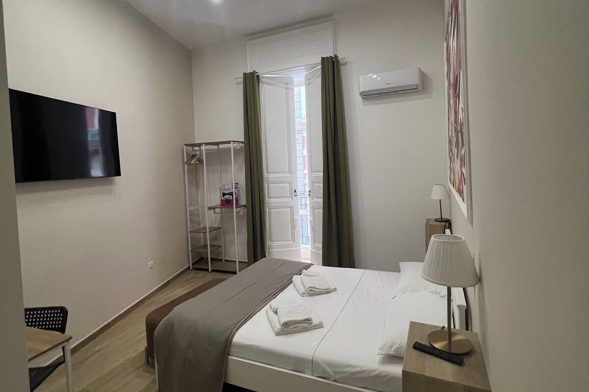 A modern hotel room with a bed, bedside table, lamp, and a TV mounted on the wall.