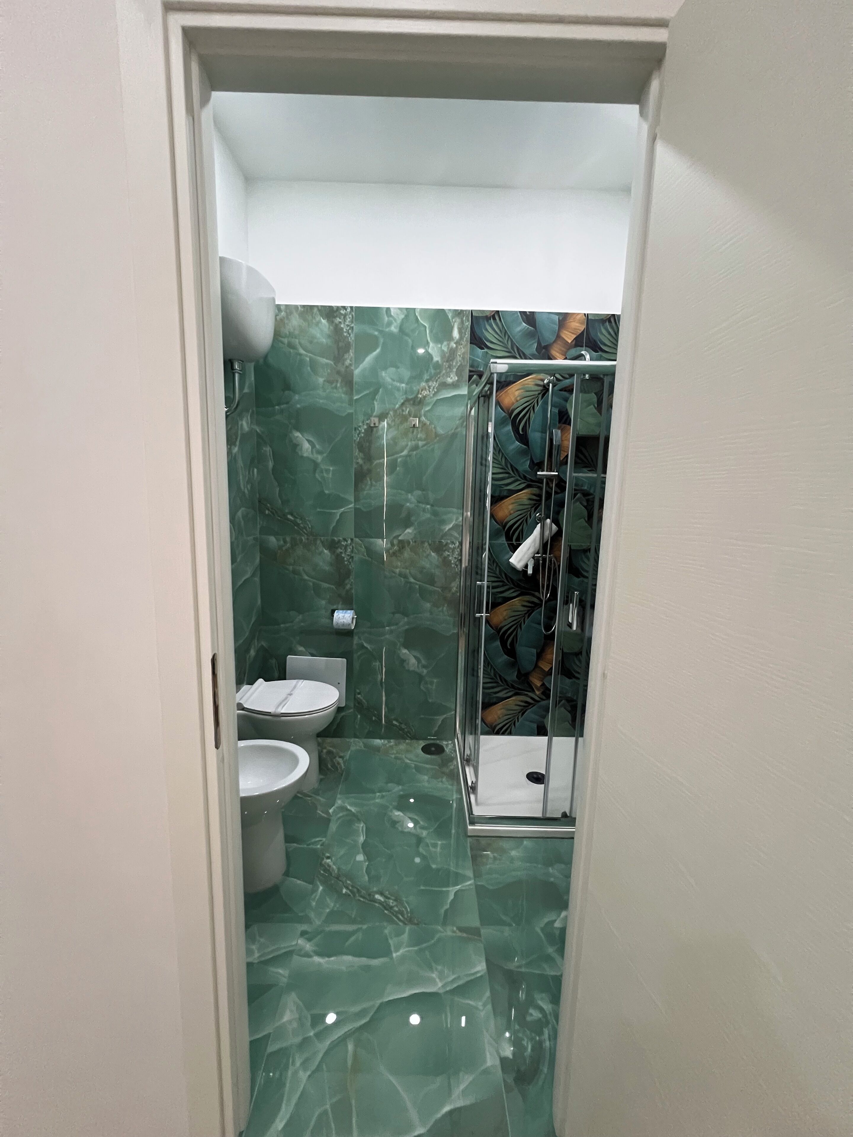 A bathroom with a marble floor, a toilet, a sink, and a glass shower enclosure.
