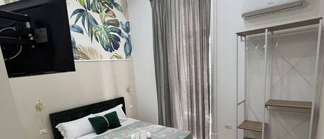 Un dormitorio con cama, escritorio, armario y aire acondicionado instalado en la pared.