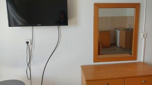 Une chambre dotée d’un téléviseur à écran plat fixé au mur, d’une commode en bois et d’un miroir qui reflète une salle de bain avec un lavabo et des placards.