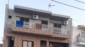 Un immeuble de deux étages doté d’un balcon, de climatiseurs et d’un escalier menant à l’entrée.