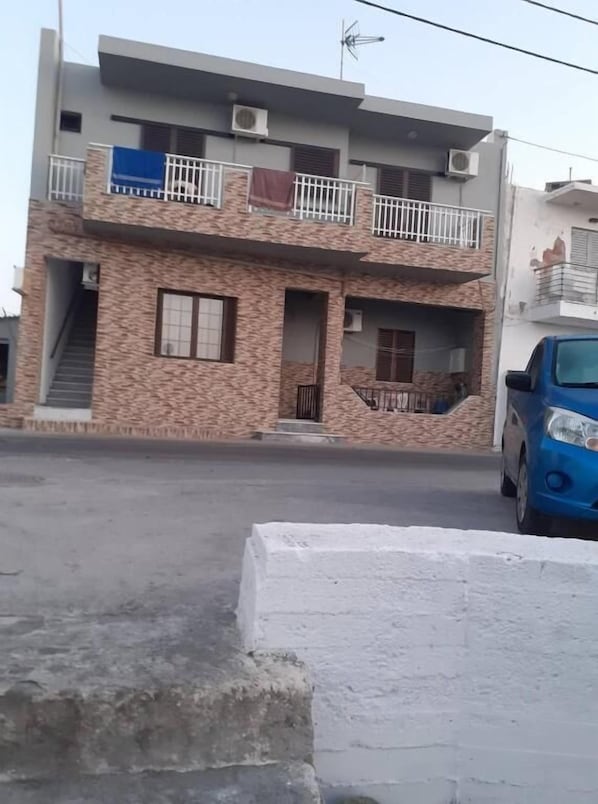 Un edificio de dos plantas con balcón, unidades de aire acondicionado y una escalera que lleva a la entrada.