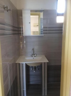 Un baño con un lavamanos blanco, un espejo encima y paredes de baldosas oscuras.