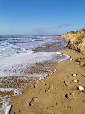 A sandy beach with footprints and rocks, a clear sky, and waves approaching the shore. - Maison Avec Jardin au Centre de L'île à Proximité des Attractions et Plages (Saint-Pierre-d'Oléron)