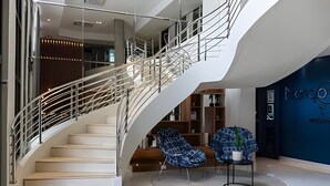 A modern interior with a curved staircase, a seating area with patterned chairs, and a blue accent wall.