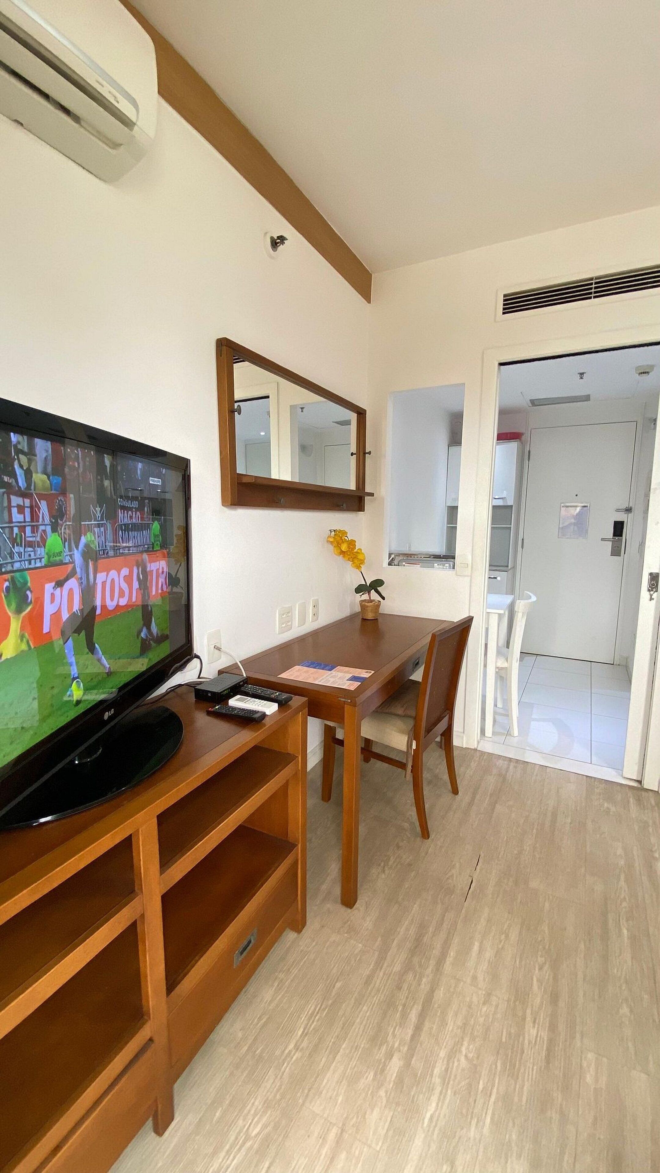 A living room with a flat-screen TV, wooden furniture, a mirror, and a door leading to another room.