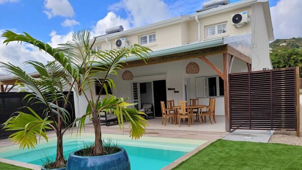 Una casa de dos pisos con piscina, mobiliario exterior y un patio cercado.