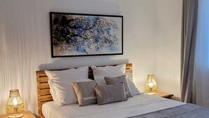 Un dormitorio con cama de madera, ropa de cama blanca, una obra de arte colgada en la pared y dos lámparas de noche.