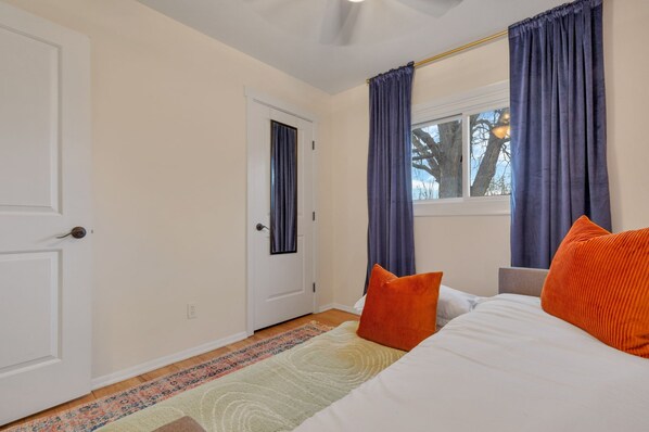 A bedroom with a bed, two pillows, a window with curtains, a door, and a patterned rug.