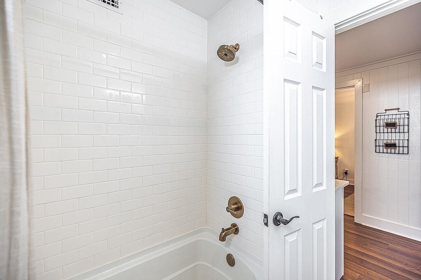 A bathroom with white subway tiles, a bathtub, a showerhead, and a door with a handle.