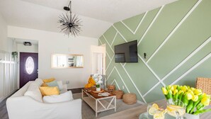 Un soggiorno moderno con un divano bianco, un tavolino e una TV montata su una parete verde.