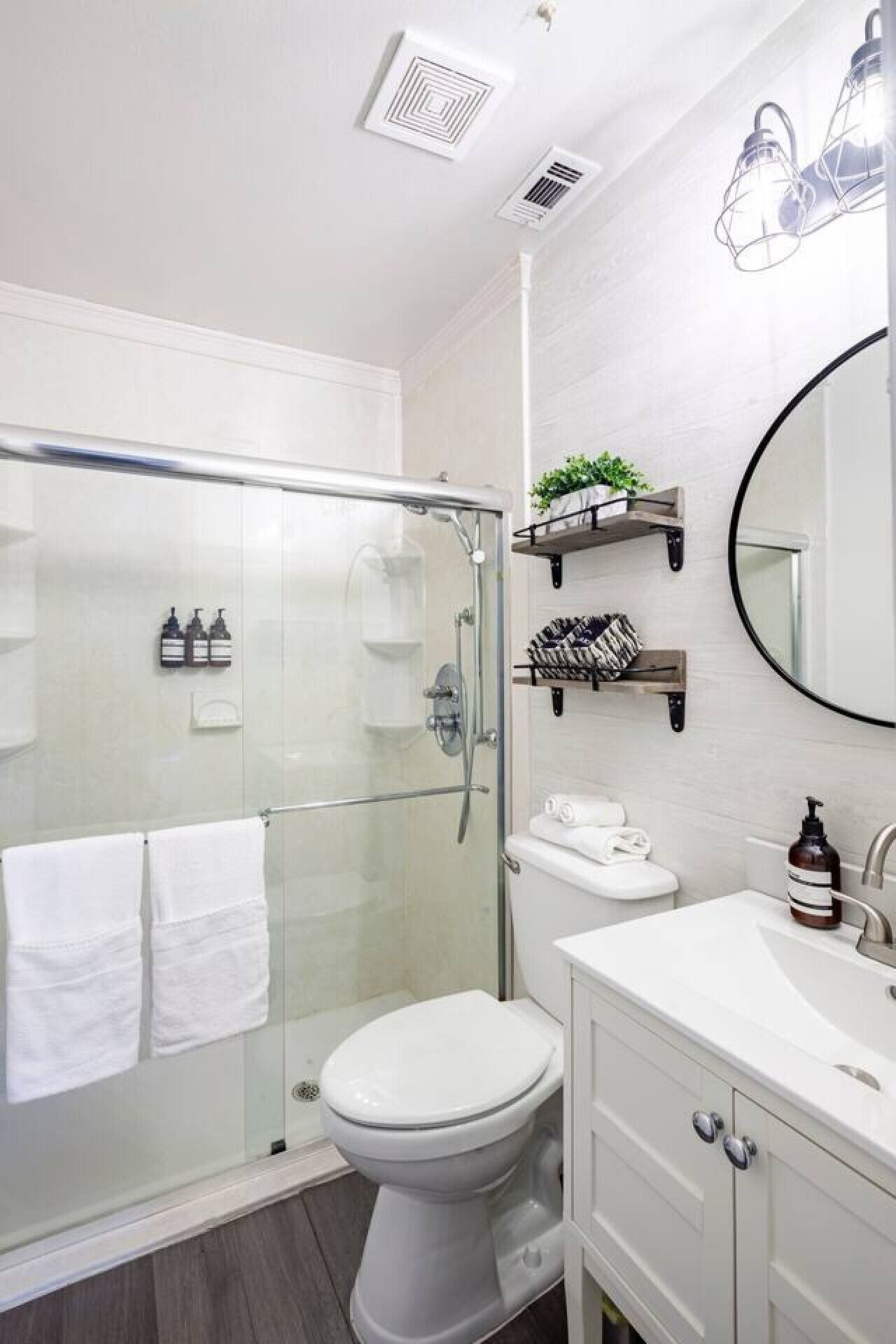 Une salle de bain moderne avec une douche à parois de verre, des toilettes, un lavabo avec un miroir et une étagère contenant des articles de toilette.