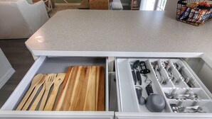 Una cucina con un piano di lavoro bianco, un organizer a cassetto con utensili in legno e un cesto di snack.