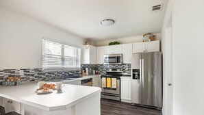 Una cucina moderna con mobili bianchi, un frigorifero in acciaio inossidabile, un forno a microonde e un forno. C'è una penisola colazione con croissant e una tazza di caffè.